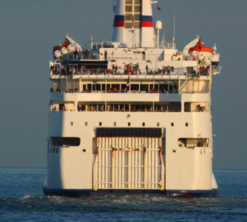 Image of a ferry sailing on the ocean with a large ship in the distance